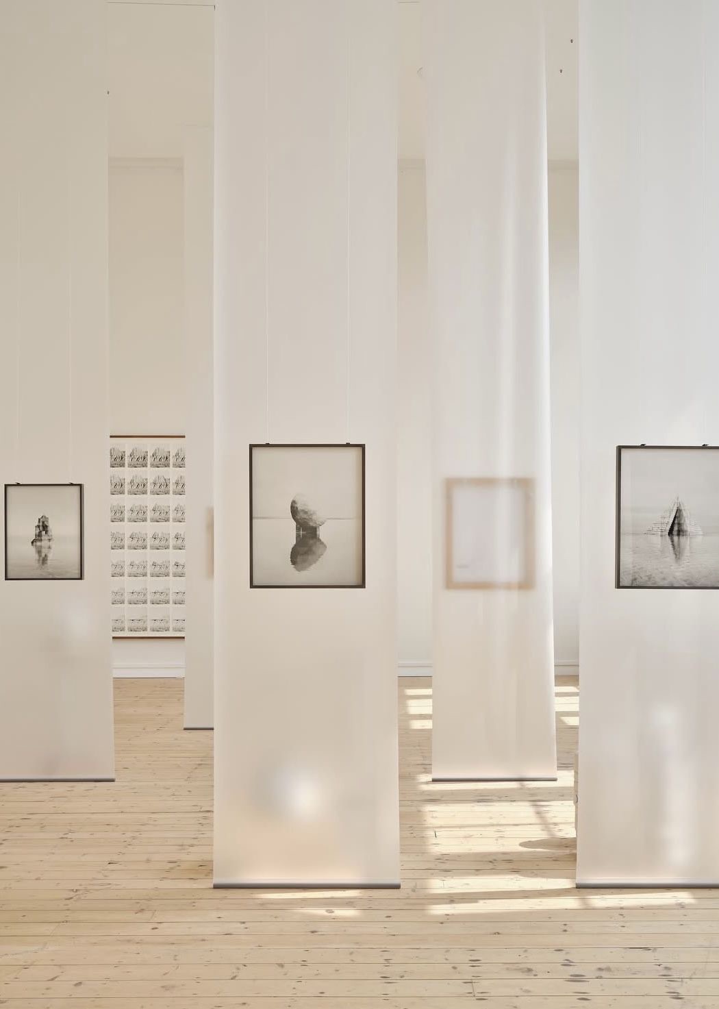 A gallery room with framed prints hanging between white curtains